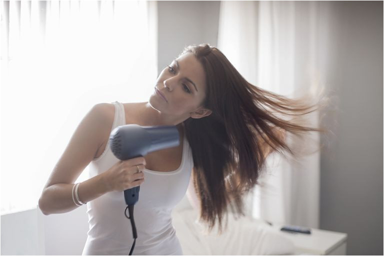 Young woman holding hair dryer drying hair